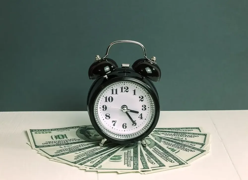 A black clock placed on top of spread out 100 dollar bills